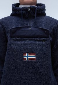 Pullover in pile blu navy con superficie testurizzata, collo con zip e tasca sul petto caratterizzata dalla bandiera norvegese in rosso, bianco e blu.