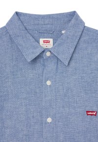 Jasnoniebieska koszula z chambray z wyraźnym kołnierzykiem, zapinana na guziki z małym czerwonym logo Levi's po lewej stronie klatki piersiowej.