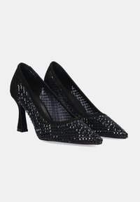 Zapatos de tacón alto negros con punta afilada, adornados con tachuelas brillantes y un tejido negro texturizado en los laterales.