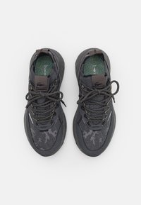 Zapatillas deportivas negras con parte superior de malla, detalles texturizados, punta redonda y cordones en contraste. Incluye una plantilla con un patrón.