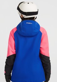 Blauwe ski-jas met roze en zwarte accenten, voorzien van een capuchon en logodetail. Gemaakt van gestructureerd, weerbestendig materiaal.