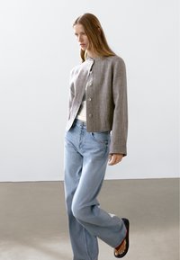 Gray, textured cropped jacket with silver buttons, worn over a white top, paired with light blue wide-leg jeans and black sandals.