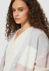 Strickjacke mit einem Farbblockdesign in sanften Pastelltönen: Grau, Rosa und Creme, mit einer strukturierten Oberfläche und Knopfdetails.