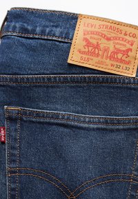 Poche arrière d'un jean en denim bleu Levi's 515 slim fit à jambe droite avec une étiquette de marque en cuir visible et une étiquette rouge Levi's.