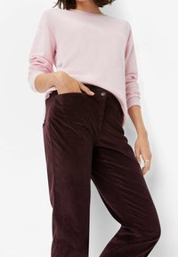 Růžový top s dlouhým rukávem spárovaný s tmavě burgundskými manšestrovými kalhotami se bočními kapsami a knoflíkovým zapínáním, které mají ribbovaný vzor.