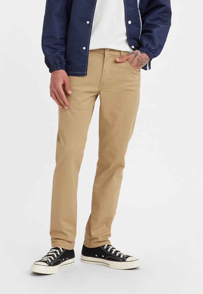 Beiga chinos med rak passform och slät bomullstyg. Kombinerade med svarta låga sneakers och en marinblå bomberjacka.