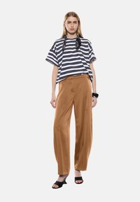 Maglietta larga a righe bianco e nera abbinata a pantaloni marroni a gamba larga e tacchi aperti neri. L'outfit presenta un design fluido e una vestibilità comoda.