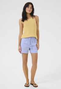 Geel gebreid mouwloos topje met een comfortabele pasvorm, gecombineerd met lichtblauwe shorts met een elastische tailleband en een trekkoord. Zwarte flip-flops.