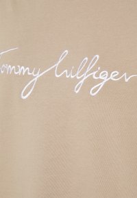 Textilie s vyraženým bílým logem "Tommy Hilfiger" v kurzívě, zdůrazňující měkkou texturu a minimalistický design.