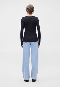 Μαύρο ριγέ μπλουζάκι με μακριά μανίκια και εφαρμοστή μέση, συνδυασμένο με ανοιχτό γαλάζιο παντελόνι wide-leg, και τα δύο εμφανίζονται από το πίσω μέρος. Απλός, μινιμαλιστικός σχεδιασμός.