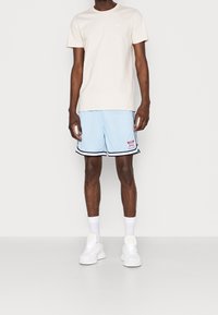 Ljusbeige bomulls t-shirt ihop med ljusblå nätshorts med svarta detaljer och en logopatch. Avslutas med vita sneakers och strumpor.