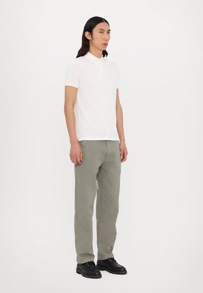 Hvid kortærmet polo shirt med krave, parret med lysegrå tapered bukser og sorte snørebåndssko. Ensfarvet baggrund.
