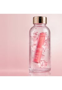 Belebender Augensticks mit Hyaluronsäure und Koffein in einer Glasflasche mit Eiswürfeln und Wassertropfen vor einem rosa Hintergrund.