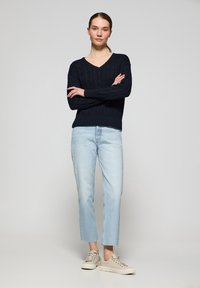 Marinblå kabelstickad tröja med djup V-ringning, kombinerad med ljusa denimcroppade jeans och beigefärgade sneakers. Fokusera på textur och passform.