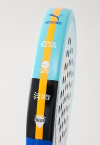 Türkisfarbene Padel-Schläger mit gelben Akzentstreifen, aus Fiberglas gefertigt, mit einer Tropfenform und verschiedenen Löchern für optimale Leistung.