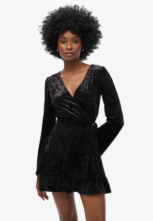 Schwarzes Samt-Wickelkleid mit langen Ärmeln, tiefem V-Ausschnitt und ausgestellt geschnittenem Saum mit Rüschendetail. Glatte Textur und figurbetonter Schnitt.