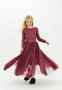 Burgundowa bluzka z długim rękawem w zestawieniu z przezroczystą, błyszczącą spódnicą z tiulu w jaśniejszym odcieniu burgundu, z wielokolorowymi, błyszczącymi akcentami.