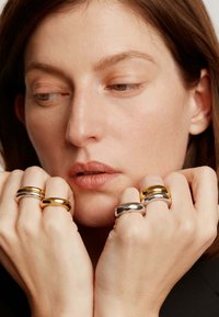 Tres anillos exhibidos en los dedos: una brillante banda de plata, una banda de oro con una curva suave y una banda de oro amarillo con un acabado pulido.