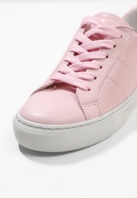 Růžové tenisky s vrchní částí z syntetické kůže, plochou bílou gumovou podrážkou a kulatou špičkou. Mají růžové tkaničky a decentní �švy.