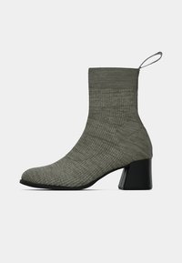 Botín de tobillo con tacón medio, parte superior de tela gris acanalada y tacón negro en bloque, con una tira en la parte trasera para tirar.