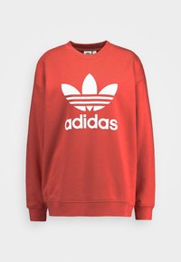 Röd sweatshirt i bomullsblandning, med en stor vit Adidas-logotyp och ikonisk trefoil-design. Ribbad halsringning och ärmslut.