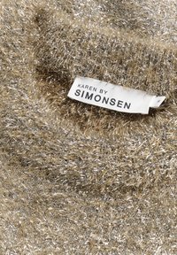 Błyszcząca tkanina w kolorze złotym i srebrnym z puszystą teksturą, z metką z napisem "KAREN BY SIMONSEN" w czarnym kolorze.