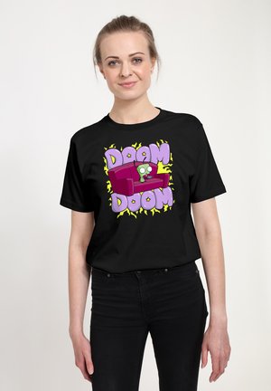 Kvinde iført sort t-shirt med tegneserieagtig grøn rumvæsen, der sidder på rød sofa, omgivet af lilla tekst "DOOM DOOM" og gule lynformer.