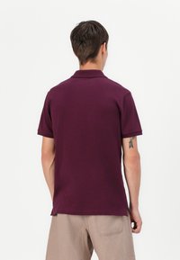 Bordeaux polo skjorte med en blød tekstur, korte ærmer og en klassisk krave. Synlige sideslids ved kanten for let bevægelse.