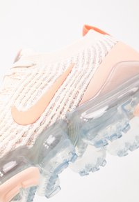 Le sneaker Nike Air VaporMax presentano una tomaia in maglia color rosa chiaro e crema, suola ad aria traslucida e il logo Swoosh color pesca.
