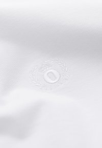 Tissu blanc texturé avec un emblème en relief subtil comprenant une couronne, une couronne de laurier et un motif circulaire au centre.