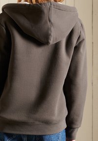 Sudadera gris con capucha ajustable, textura suave y puños acanalados. Presenta un corte relajado y costuras visibles a lo largo de las costuras.