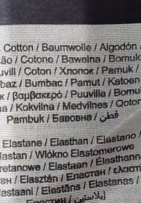 Etykieta z wieloma językami, zawierająca informacje o składzie tkaniny: bawełna i elastan, czarny tekst na teksturowanym jasnym tle.