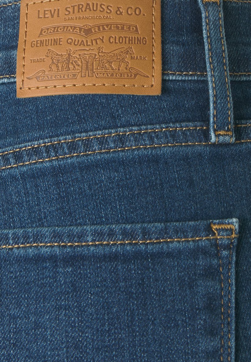 Vaqueros de denim azul oscuro con un parche de cuero con logotipo en relieve y costuras decorativas a lo largo de los bolsillos y costuras.