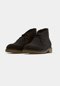Bottines en daim marron avec bout rond, design à lacets et semelle en caoutchouc flexible; présentent une bordure cousue le long du bord de la semelle.