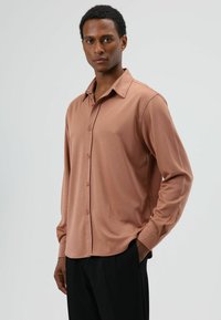 Langärmliges Hemd mit Knöpfen aus weichem, gedämpftem braunem Stoff. Verfügt über einen klassischen Kragen, durchgehende Knopfleiste und lockere Passform. Glatte Textur.