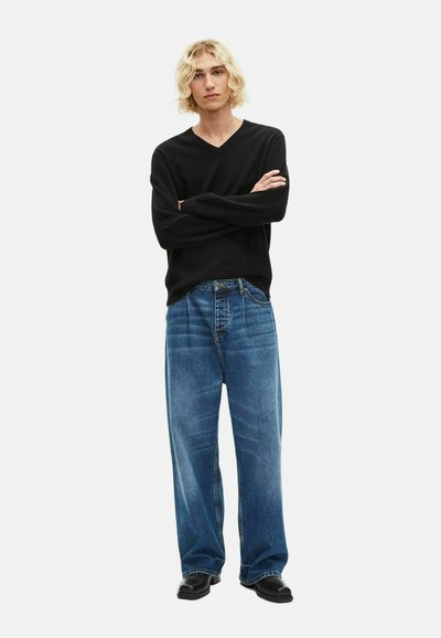 Schwarzer, langärmeliger V-Ausschnitt-Pullover, kombiniert mit lockeren, hellblauen Denim-Jeans und ergänzt durch schwarze Schuhe.
