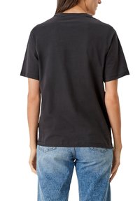 Svart bomullströja med korta ärmar, rund halsringning och avslappnad passform, i kombination med ljusblå denimjeans.