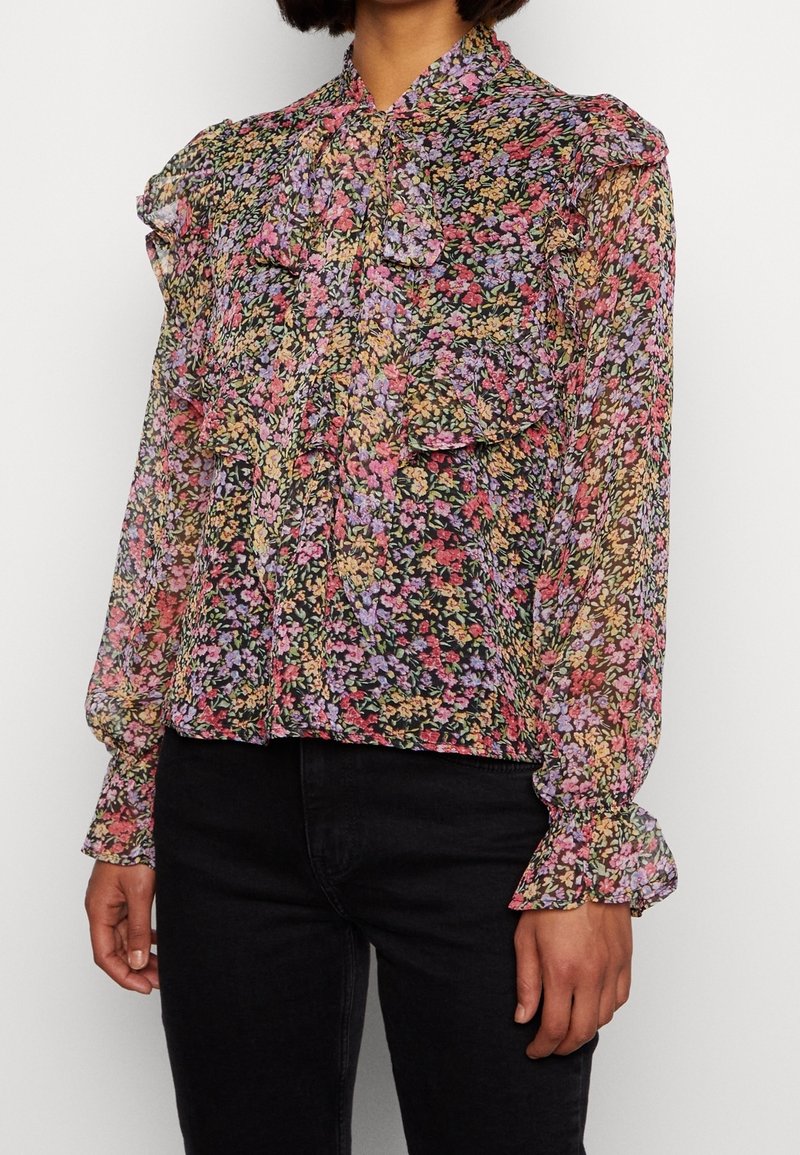 Bloes met bloemenprint van doorschijnende zwarte stof met roze, paarse en gele bloemen. Beschikt over een gerimpelde kraag en mouwen met elastische manchetten.