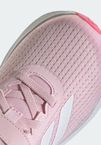 Scarpa sportiva rosa chiaro con tomaia in rete testurizzata, dettagli bianchi e suola ammortizzata. Presenta lacci piatti e punta rinforzata.