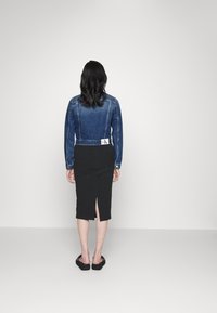 Jeansjacka med en kort design och blå gradient; kombinerad med en svart midi-kjol med en slits bak. Enkla svarta skor.