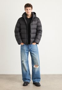 Black puffer jacket with a hood and quilted design, paired with light blue ripped wide-leg jeans and black shoes.