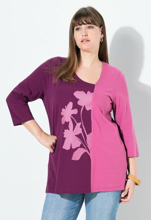 Lilla og lyserød langærmet top med et blomstermønster på den lilla side; har en V-hals og en løs pasform. Struktureret stof med sideslids.