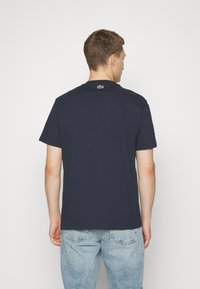 Camiseta de algodón azul marino de mangas cortas, con cuello redondo y un pequeño logo verde en la parte posterior. Presenta un diseño de corte relajado.