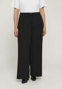 Pantalones de pierna ancha negros, hechos de una tela suave, con pliegues frontales y cierre de botón. Combinados con una blusa blanca sencilla.