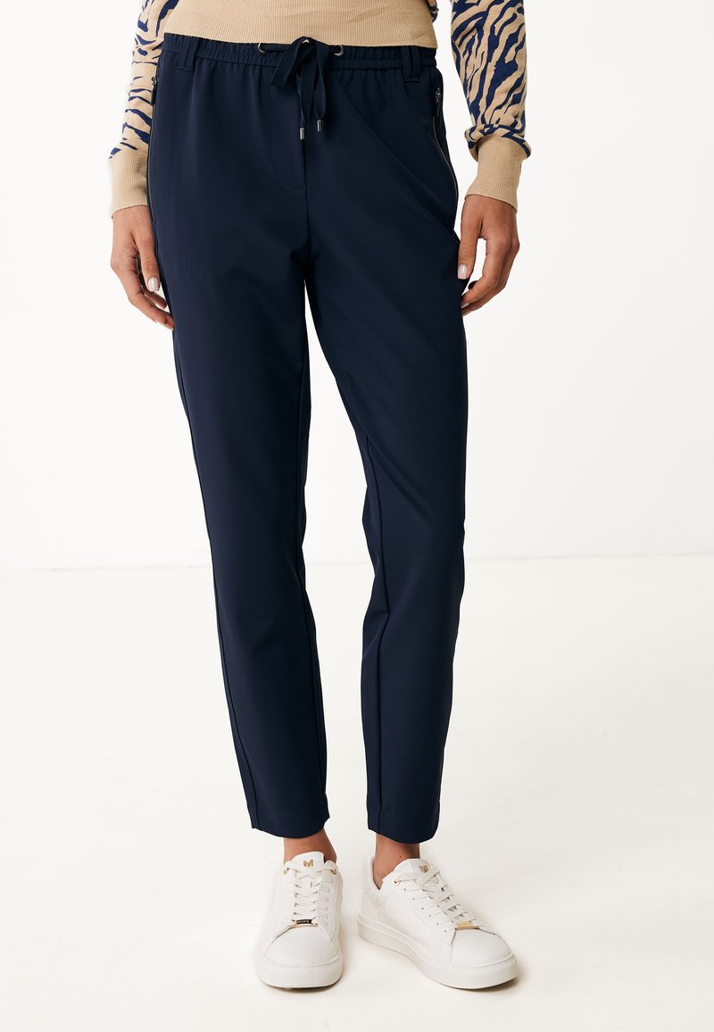 Pantalones ajustados de color navy con cinturilla elástica y cordón. Cuentan con bolsillos laterales con cremallera y están hechos de una tela suave y ligera. Combinados con zapatillas blancas.