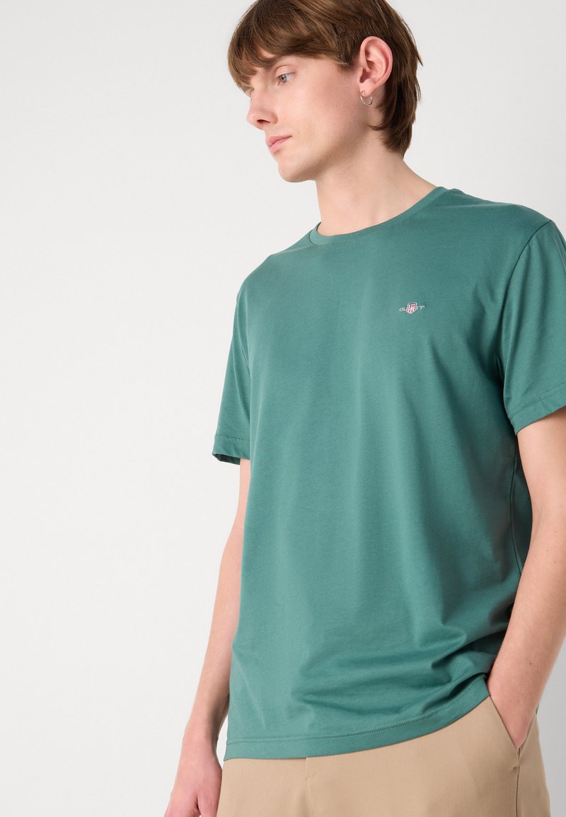 Grünes Baumwoll-T-Shirt mit Rundhalsausschnitt, kurzen Ärmeln und dezent gesticktem Logo. Sanfte Textur und entspannter Schnitt.