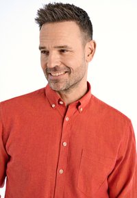 Czerwona koszula zapinana na guziki, wykonana z teksturowanej tkaniny, z kieszonką na klatce piersiowej i jasnymi guzikami. Kołnierz ma ostry fason.