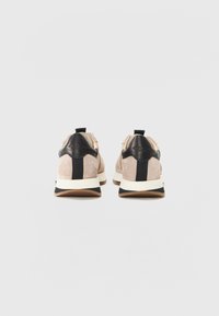 Tan suede sneakers with a black leather heel, elastic accents, and a white midsole. Rear view showcases a prominent pull tab and contrasting textures.