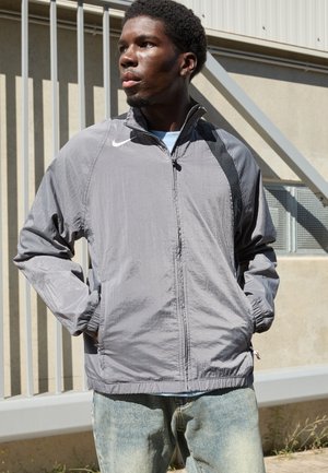 Gray lightweight jacket with a high collar, zip front, elastic cuffs, and side pockets. Features a small white Nike logo on the chest.