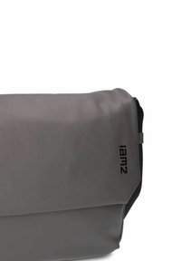Borsa a tracolla grigia realizzata in materiale liscio e impermeabile, con fodera ripiegata e un logo nero stampato sul lato.